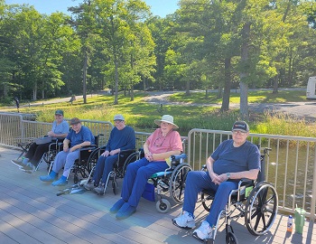 Nursing Home Patients getting some fresh air outside near the water. There is five people sitting down in wheelchair's